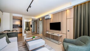A modern living room with a flat-screen TV, green upholstered sofas, a coffee table, and a dining area with a kitchen in the background. - Casamax Suites (Konyaalti)