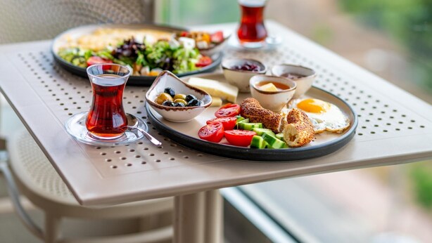 A balcony table with a meal setup including plates, bowls, and a glass of red beverage. - Casamax Suites (Konyaalti)