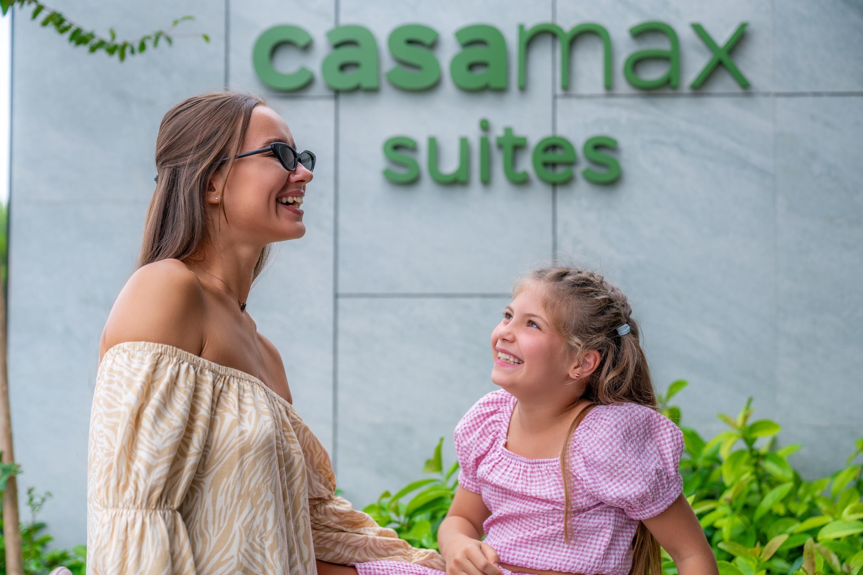 En kvinde og en ung pige foran et skilt, der siger 'casamax suites'.