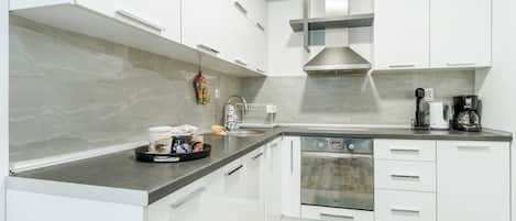 A modern kitchen with white cabinets, a stainless steel range hood, a built-in oven, and a coffee maker.