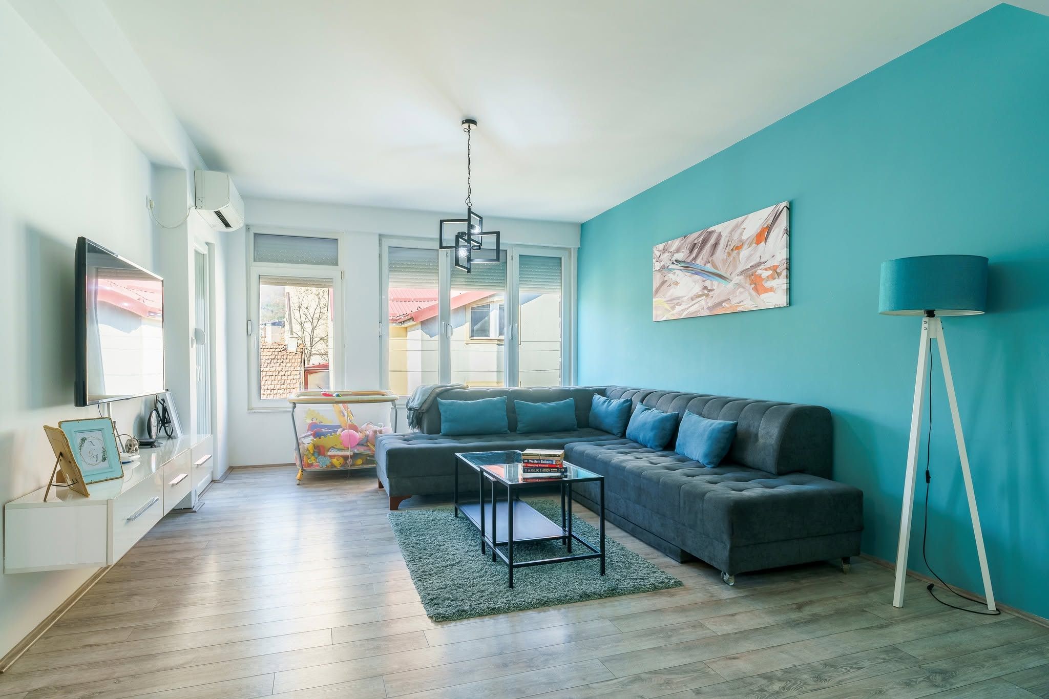 Un salon moderne avec un canapé gris, une table basse en verre et un mur d’accent bleu.