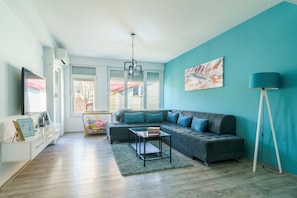 A modern living room with a grey sofa, a glass coffee table, and a blue accent wall. - L&L Apartments - Harmony Residence Bitola (Bitola)