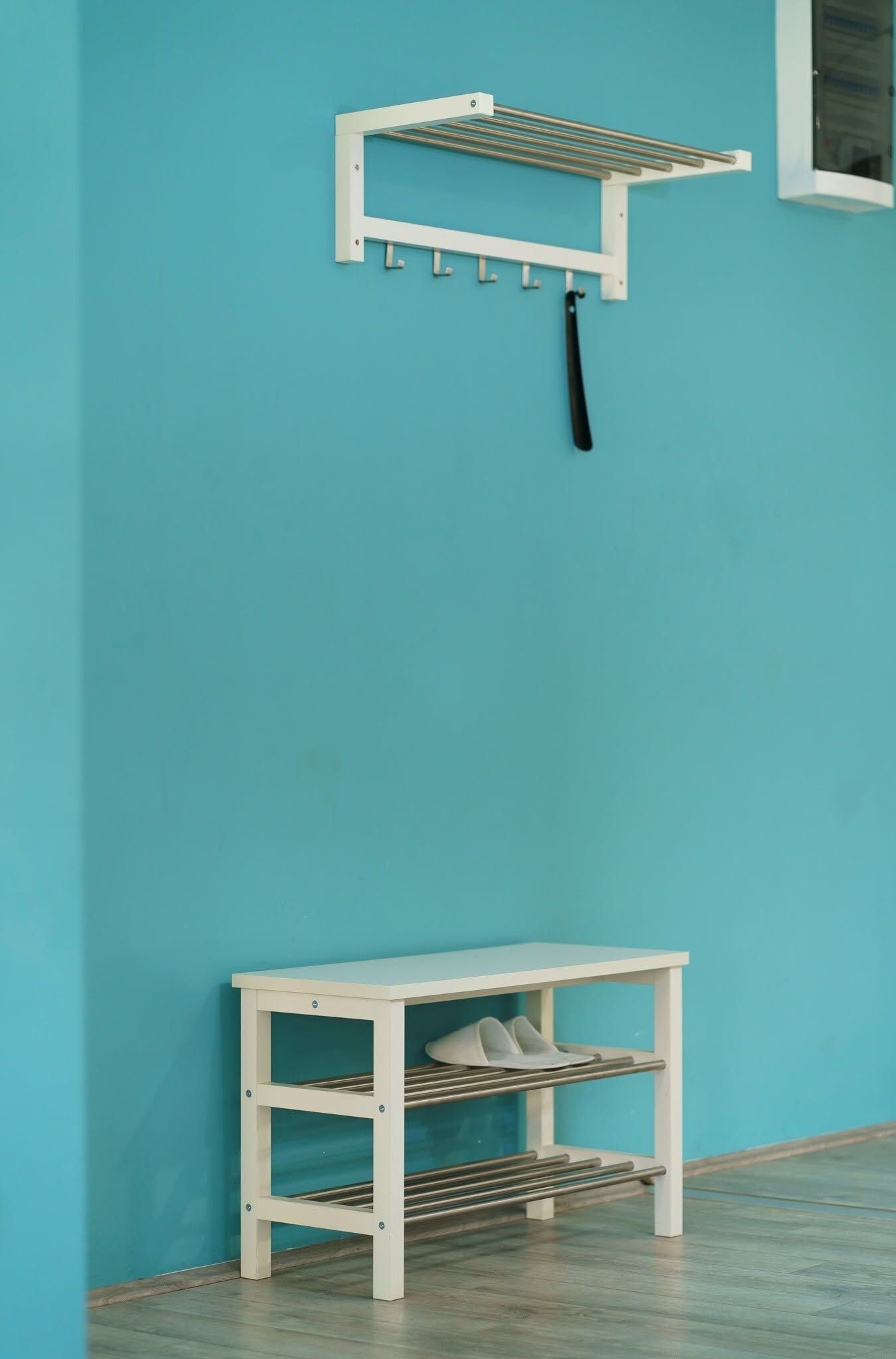 A white metal shelf unit with a hanging rack and a lower shelf with shoes against a teal wall.