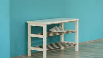 A white metal shelf unit with a hanging rack and a lower shelf with shoes against a teal wall.