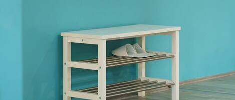 Une étagère métallique blanche, dotée d’une barre de suspension et d’une étagère inférieure où sont rangées des chaussures, le tout placé devant un mur de couleur turquoise.