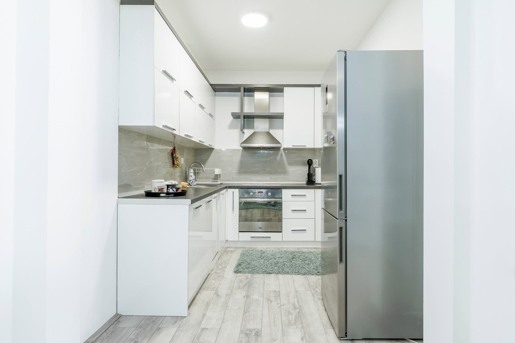 A modern kitchen with white cabinetry, a stainless steel refrigerator, a built-in oven, and a microwave.