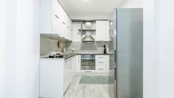 A modern kitchen with white cabinetry, a stainless steel refrigerator, a built-in oven, and a microwave.