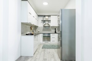 A modern kitchen with white cabinetry, a stainless steel refrigerator, a built-in oven, and a microwave.