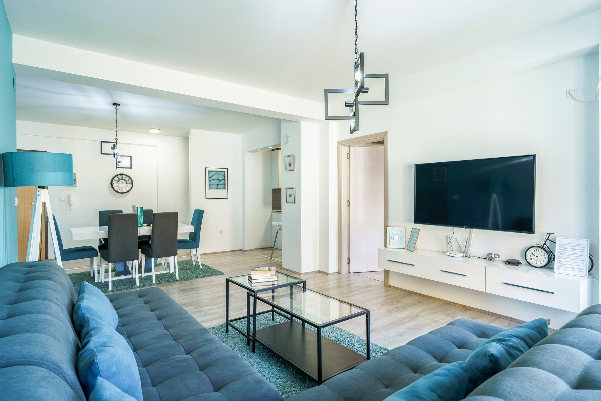 A modern living room with a sofa, a coffee table, a TV, and a dining area with chairs and a table.