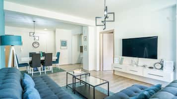 A modern living room with a sofa, a coffee table, a TV, and a dining area with chairs and a table.