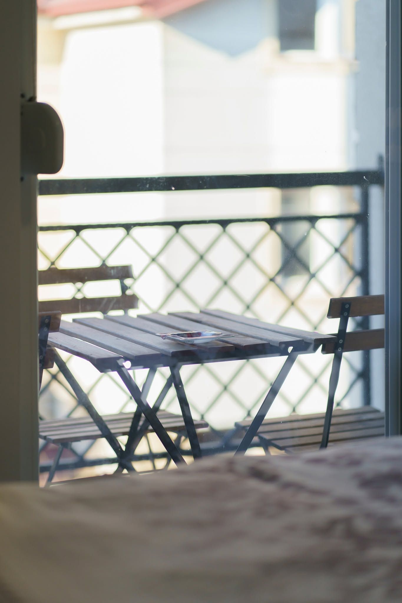 En balkon med et bord og stole, gelænder i metal og udsigt til bygninger.
