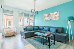 A modern living room with a grey sectional sofa, a glass coffee table, and a teal accent wall. - L&L Apartments - Harmony Residence Bitola (Bitola)