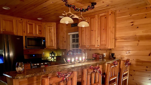 Cocina de cabaña de madera con una isla central, taburetes de bar, un refrigerador, microondas y una ventana.