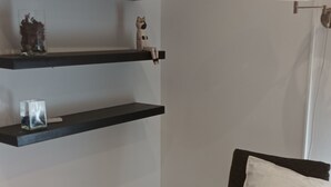 Ein Zimmer mit Holzstuhl und Sitzkissen, einem kleinen Holztisch und Regalen mit Dekoration.
