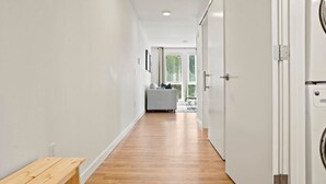 Kapea käytävä, jossa on puulattia, valkoiset seinät ja penkki vasemmalla puolella. Oikealla puolella olevat ovet johtavat pyykinhuoltotilaan.