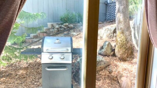 En grill i en trädgård med en träaltan, en stenmur och ett träd.