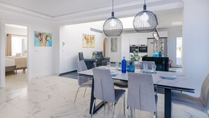 Un'elegante zona pranzo moderna con pavimento in marmo, sedie rivestite in grigio e un tavolo da pranzo nero. Due lampade a sospensione illuminano il tavolo.