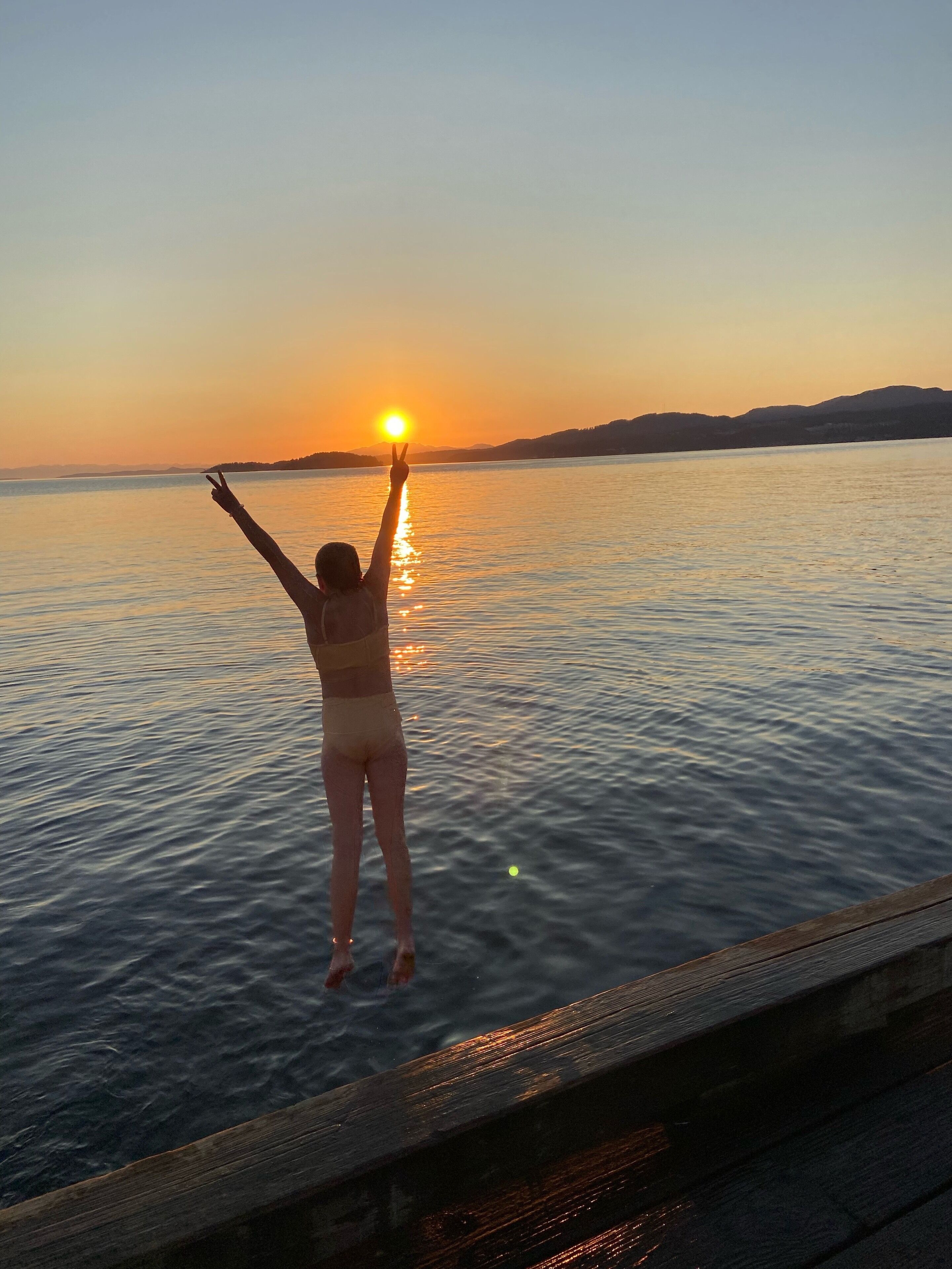 Una persona de pie en un muelle, mirando una puesta de sol sobre el agua.