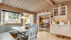 A modern kitchen with wooden cabinetry, a dining area with a table and chairs, and a view through an open door to a living room.