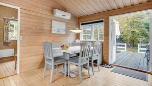 A wooden cabin interior with a dining table, chairs, and a large window offering a view of the outdoors.
