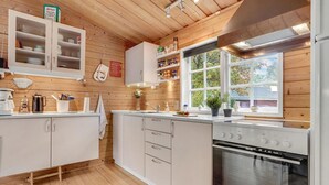 A modern kitchen with wooden walls, white cabinets, a built-in oven, and a window with a view of trees.