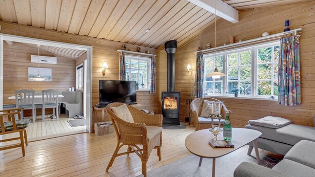 A cozy cabin interior with a fireplace, wicker furniture, a dining area, and large windows offering a view of the outdoors.