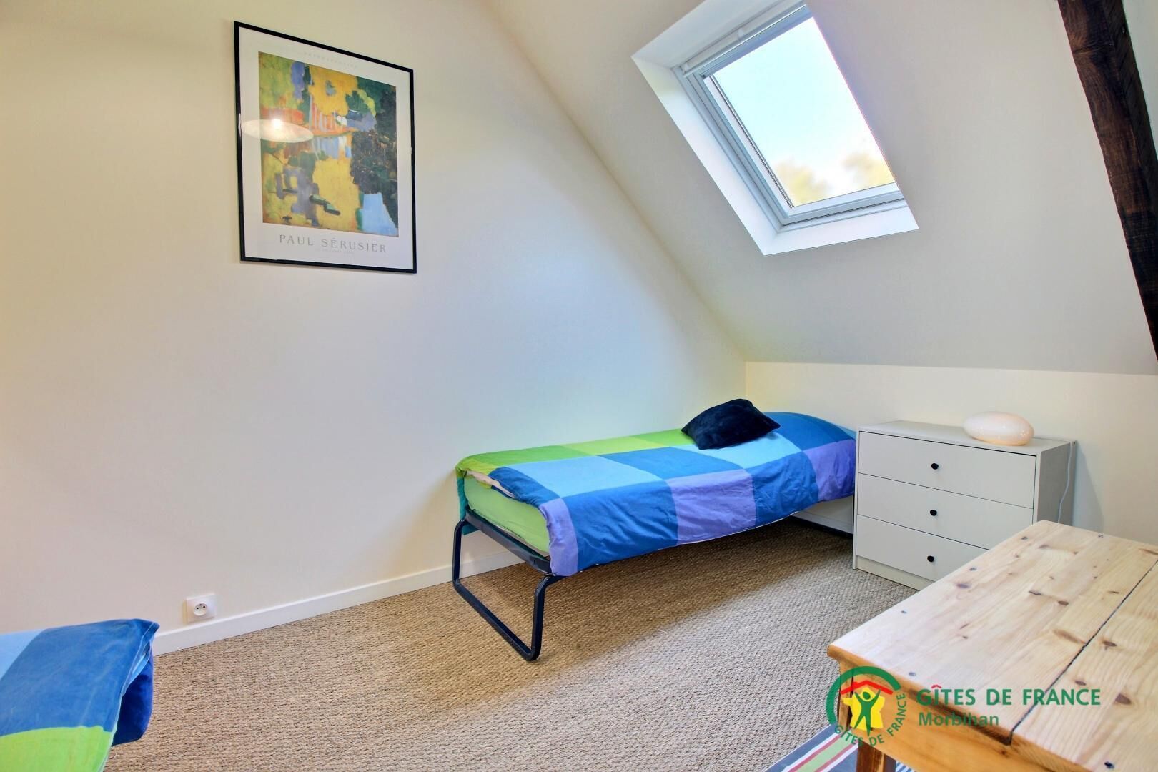 A small, neatly arranged bedroom with a bed, a dresser, a window, and a framed picture on the wall.