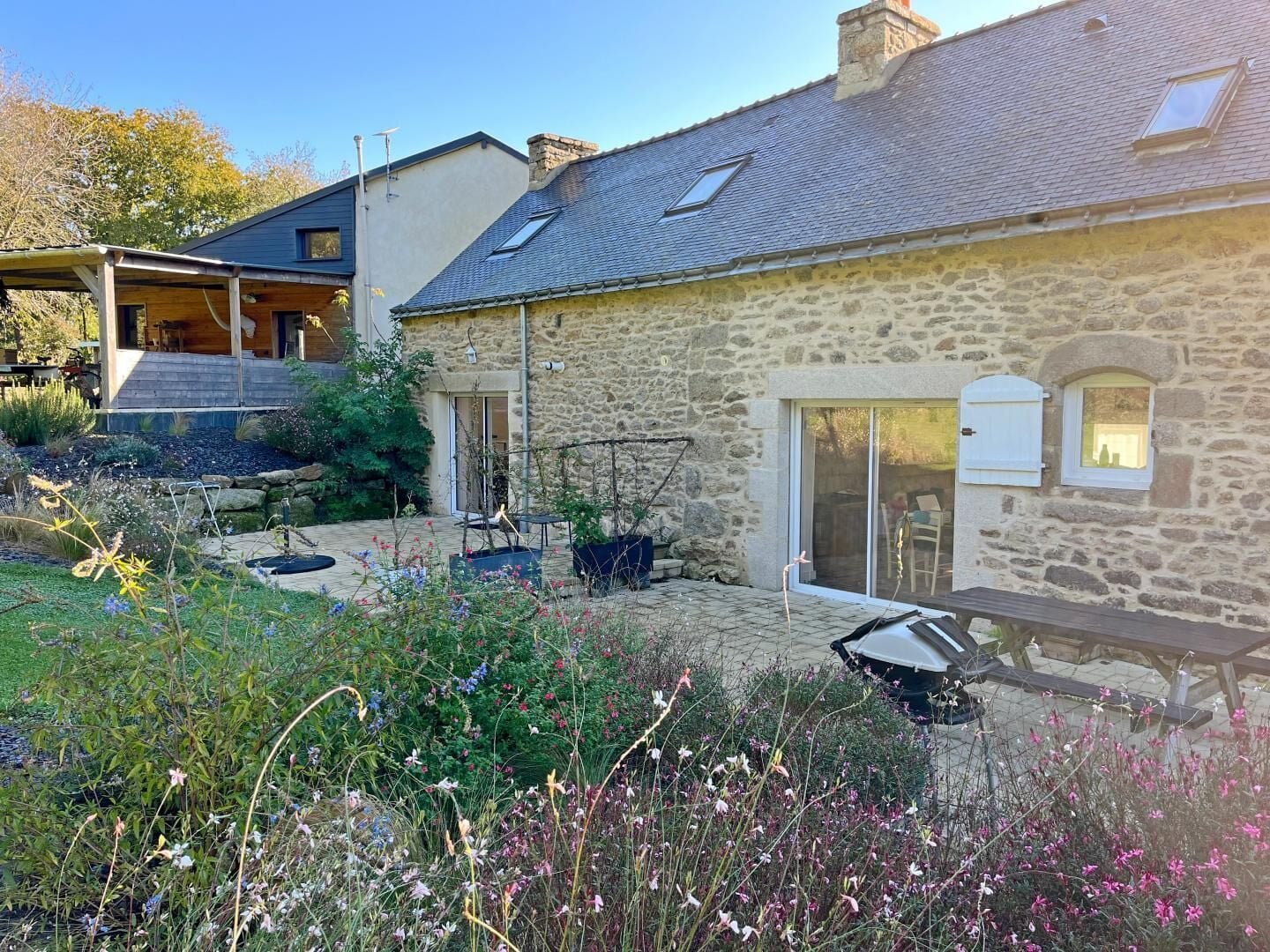 Une maison en pierre avec un jardin, une terrasse avec une table et des chaises, et un espace extérieur aménagé et couvert.