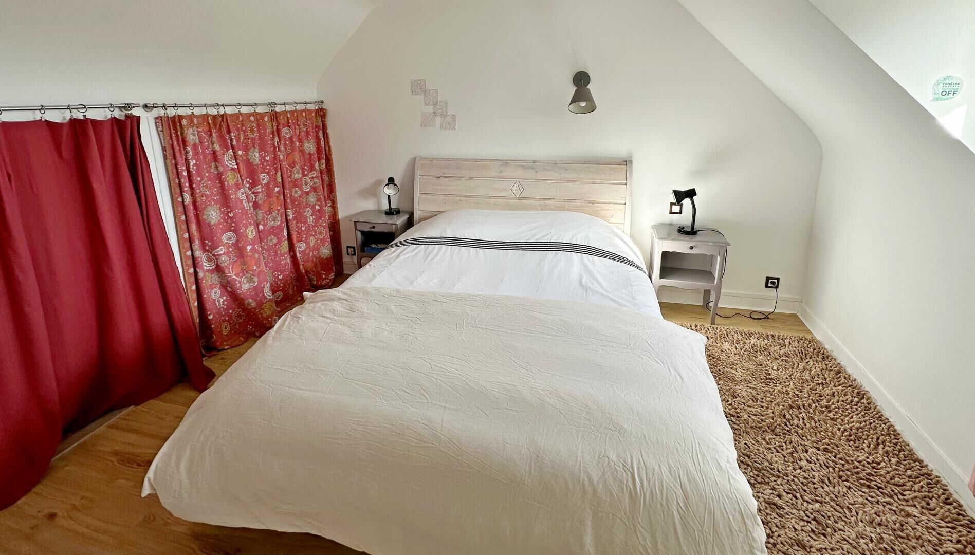 Una camera da letto con un letto grande, una testata imbottita in legno, due comodini con lampade, una tenda rossa e una tenda decorata.