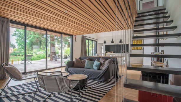 Un salon moderne avec un plafond en bois, de grandes fenêtres, un canapé, une table à manger et un escalier.