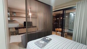 A modern hotel room with a bed, a desk, a chair, and a balcony with a view of the city at night. - Kazanoah - Campo Belo (São Paulo)