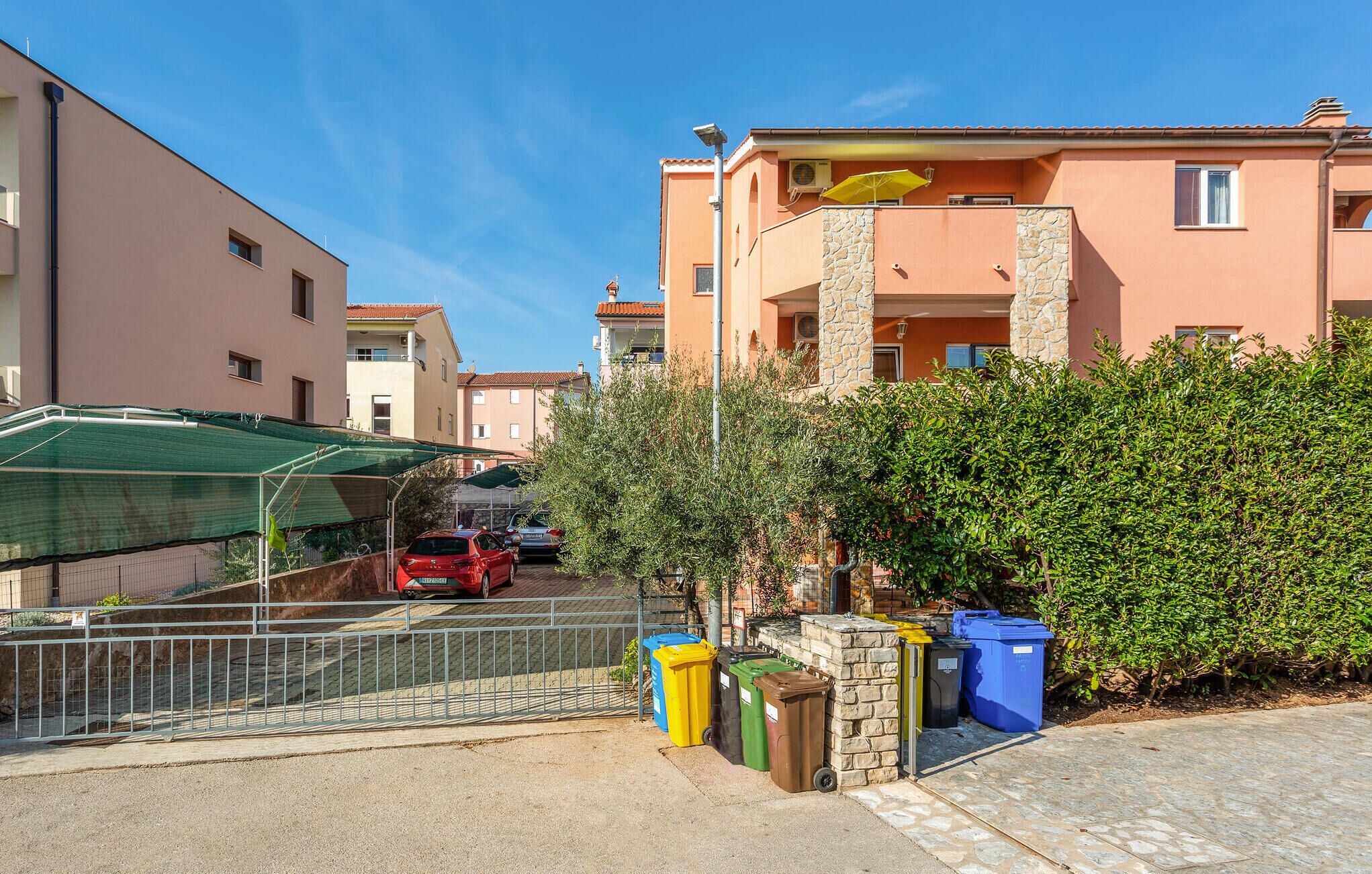 A residential area with a row of apartment buildings, a parked car, and a row of trash bins.