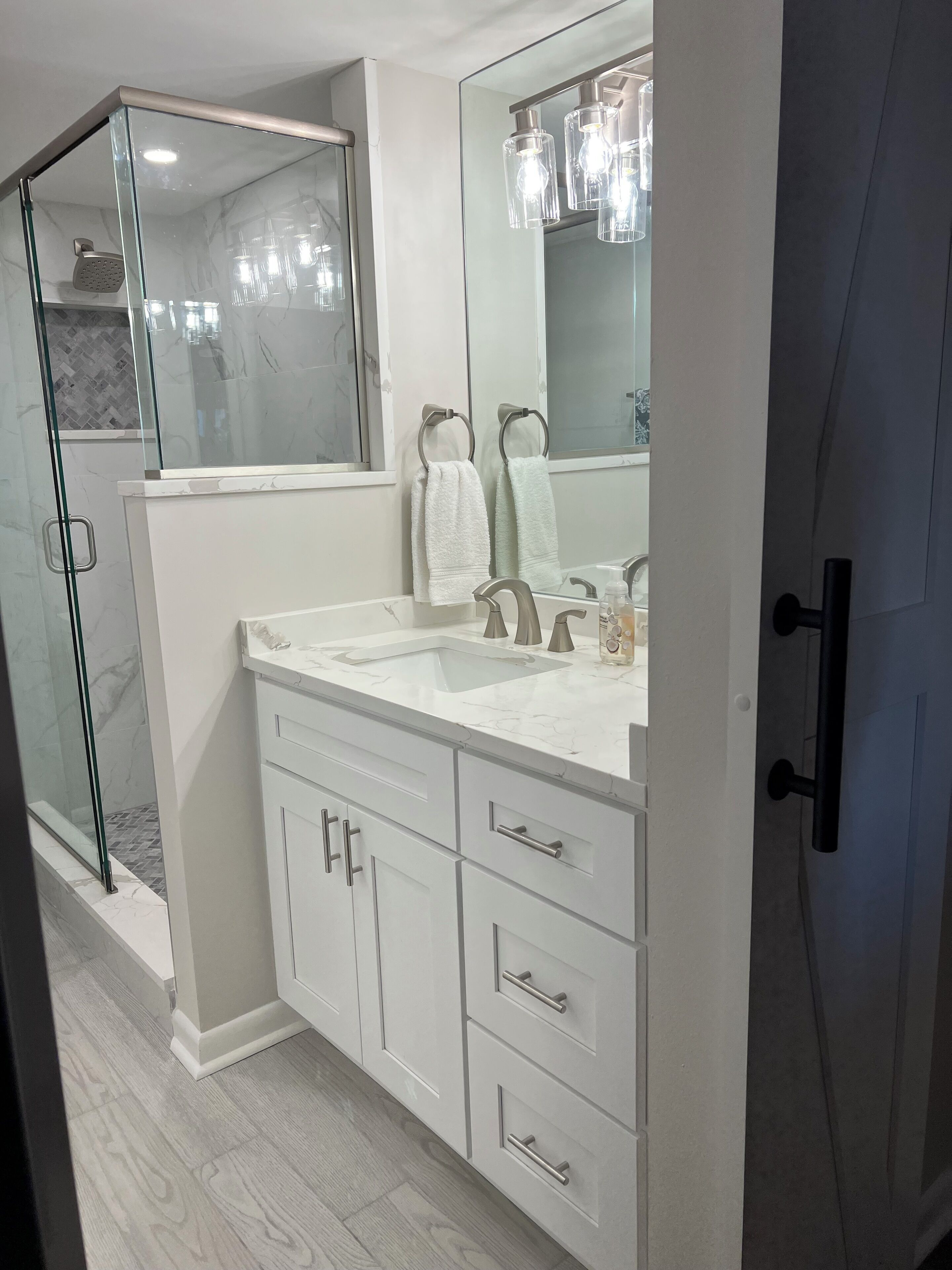 A modern bathroom with a glass shower enclosure, a large mirror, and a double sink vanity with drawers.