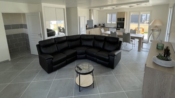 Ein modernes Wohnzimmer mit einem Ecksofa, einem Glastisch und einer Essecke mit Tisch und Stühlen.