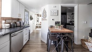 Ett modernt kök med vita skåp, en bänkskiva i trä och en matplats med ett träbord och barstolar.