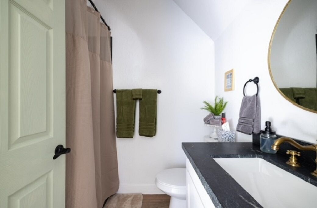 A bathroom with a white toilet, a black sink with a gold faucet, and a green towel hanging on a rack.