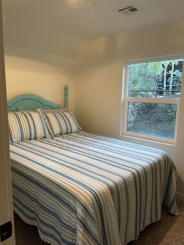 A bed with a striped bedspread, a headboard, and a window with a view of trees and a fence.