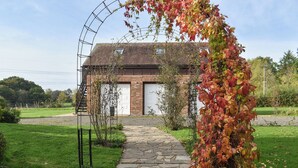 Een pad van stenen loopt naar een bakstenen gebouw met een garagepoort, omgeven door groen en een metalen boog.