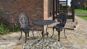 Een terras met een bakstenen muur, twee sierlijke metalen stoelen, een ronde tafel en een houten pergola.