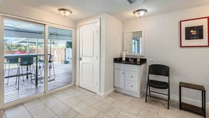 A room with a sliding glass door leading to an outdoor patio, a white vanity with a mirror, a black chair, and a framed picture on the wall.