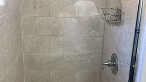 Un área de ducha con paredes de azulejos, un cabezal de ducha, una barandilla y un estante metálico.