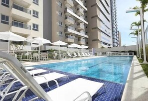 A swimming pool with lounge chairs and umbrellas, surrounded by a high-rise building with balconies.
