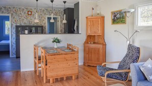 Ein gemütliches Wohnzimmer mit einem Holzesstisch, einem blauen, gemusterten Sessel und einer Holzkommode.