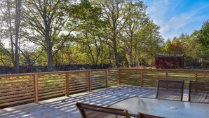 Eine Holzterrasse mit Tisch und Stühlen, umgeben von einem Holzzaun und Bäumen.