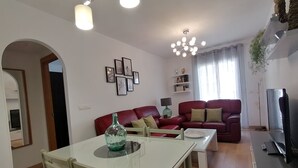 A living room with a red sofa, a dining table with chairs, a chandelier, and a TV stand. - Relax & Home, Apartment with terrace and parking (La Zubia)