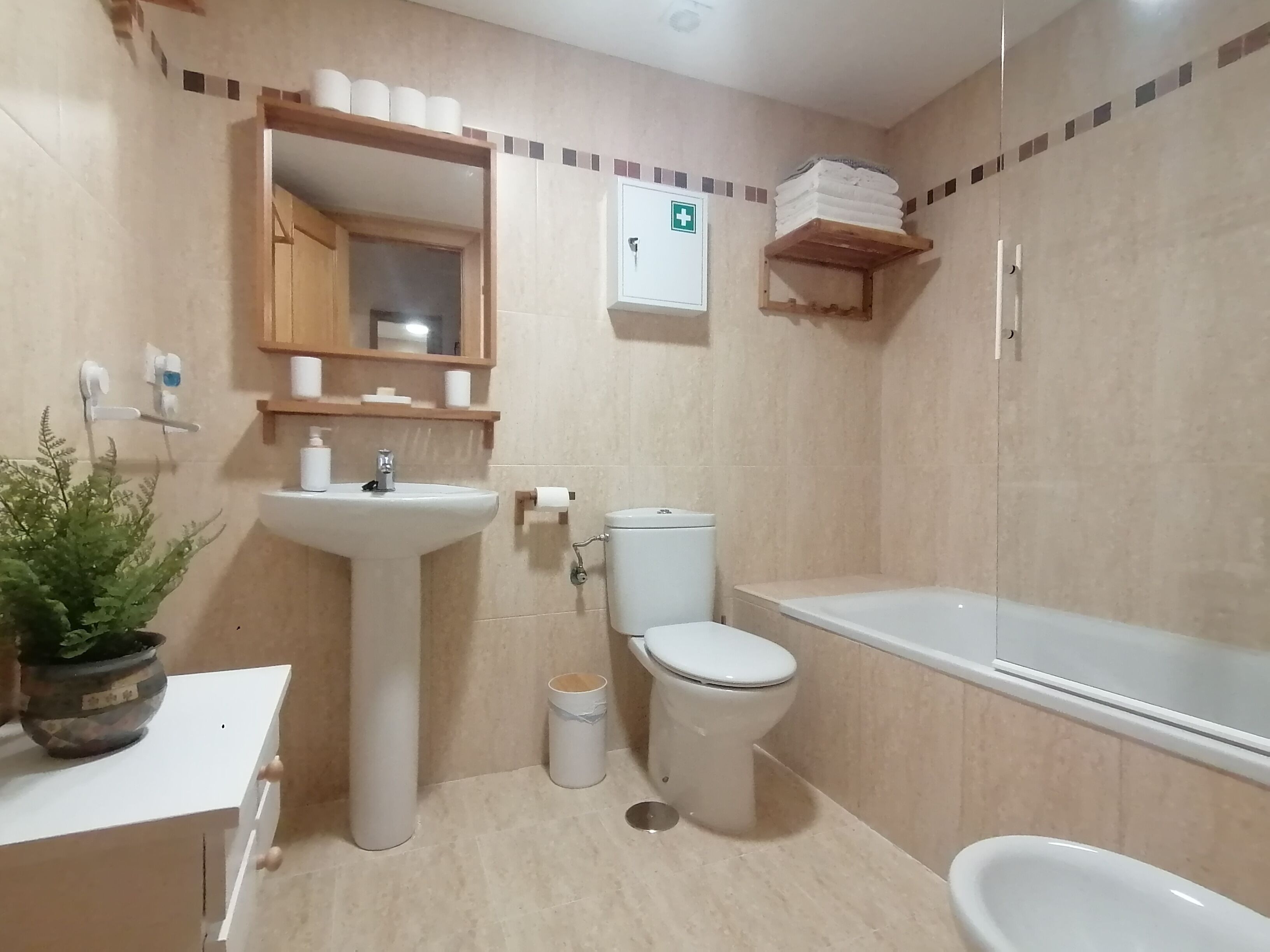 Ein Badezimmer mit Waschbecken, Toilette und Badewanne. Über dem Waschbecken hängt ein Spiegel, und darunter befindet sich ein kleines Regal mit Handtüchern.