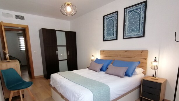 A bedroom with a bed, bedside tables, a chair, a wardrobe, and two wall-mounted lights. - Relax & Home, Apartment with terrace and parking (La Zubia)