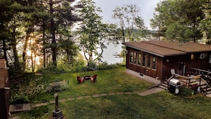 Uma cabana com varanda, um espaço de estar ao ar livre e vista para um lago.