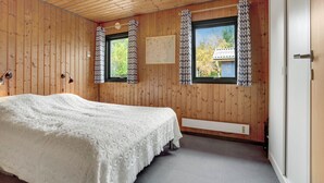 Ein Schlafzimmer mit Holzwänden, einem Bett mit weißer Decke, zwei Fenstern mit gemusterten Vorhängen und einer Karte an der Wand.