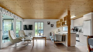 Ein geräumiger Wohnbereich mit Holzbalkendecke, einem an der Wand befestigten Fernseher, einem Sofa, einem Couchtisch und einer Küchenzeile mit modernen Geräten.